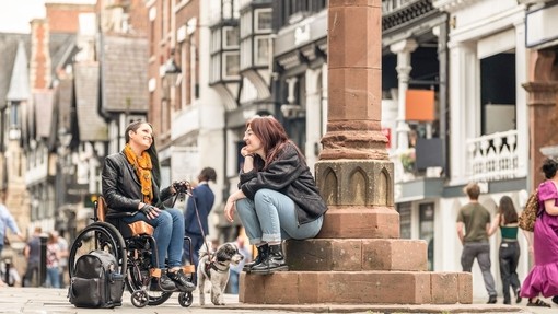 Two women sit talking together in a town centre