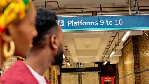 A couple look up at sign for Platforms 9 and 10 at a train station