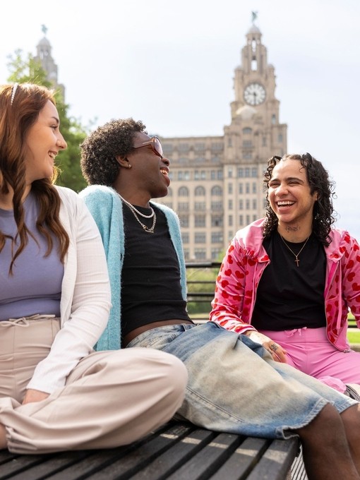 A group of friends sit together on a bench in front of an iconic building