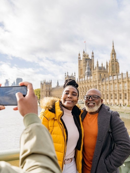 A man photographing mature couple with a large river and iconic buildings in the background.
