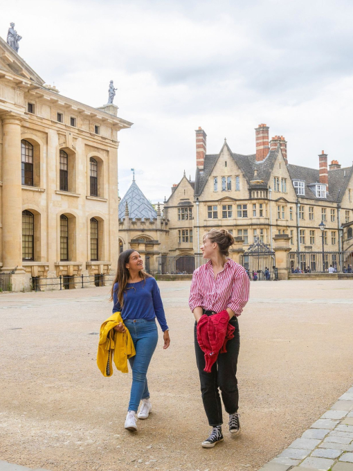 Two women walk across a courtyard among heritage buildings