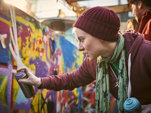 One young woman using aerosol to create street art mural