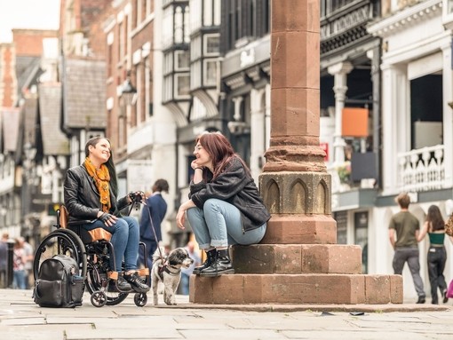 Two women sit talking together in a town centre