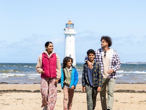 Family walk along a beach with a lighthouse in the background