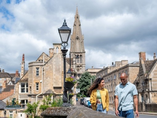 A man and a woman walk through a stone built village with a church