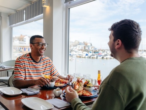 Two men eat lobster in a restaurant with a harbour view