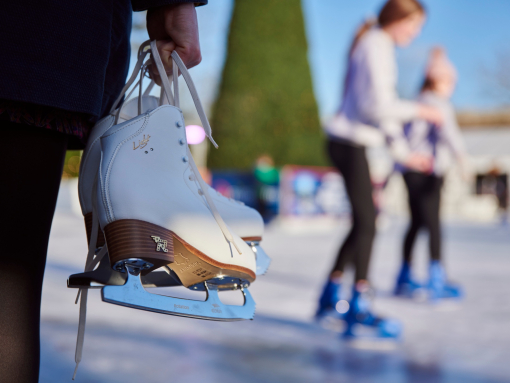 Hands holding a pair of white ice skates by the laces