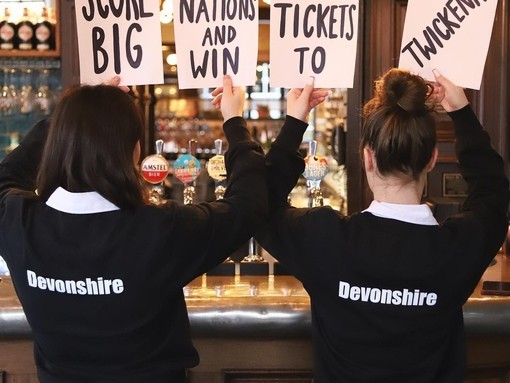 Two female staff from Devonshire Balham Public House holding signs for free tickets to Six Nations Rugby, Twickenham