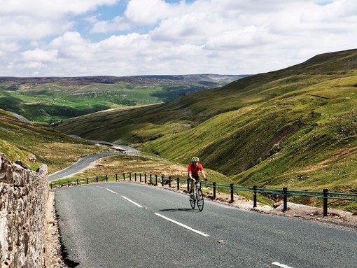 Cyclist riding on road through green dales