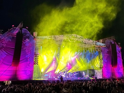 A crowd of people in front of the stage of a musical festival at night.
