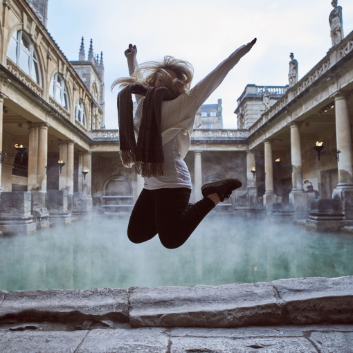 Woman leaping in the air at The Roman Baths, Bath, Somerset, England.