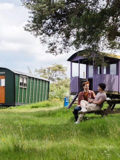 Two men sat oustide a shepherds hut in the countryside