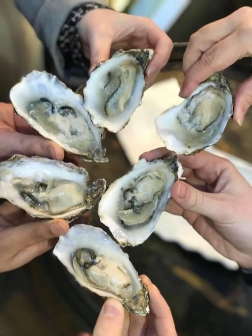 Close-up of six hands holding open oyster shells complete with oysters, ready to eat