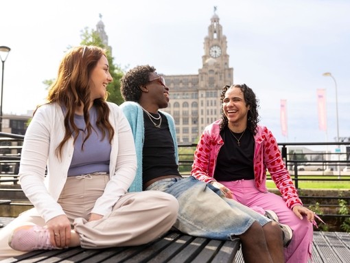 A group of friends sit together on a bench in front of an iconic building