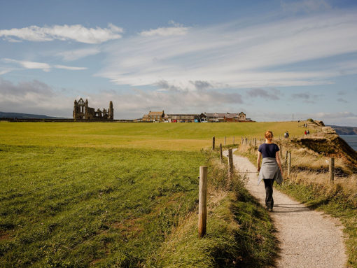 Woman walking along a coastal path towards a ruined abbey