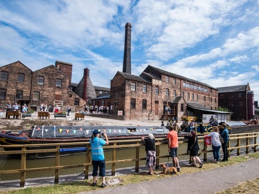 A group of people looking across the Trent and Mersey Canal at several historic buildings in Stoke