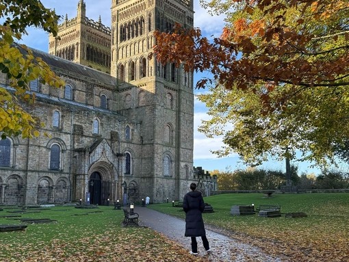 A woman in a warm jacket facing a large cathedral and tower.