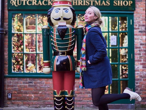 Woman posing beside a nutcracker prince statue, outside a christmas shop