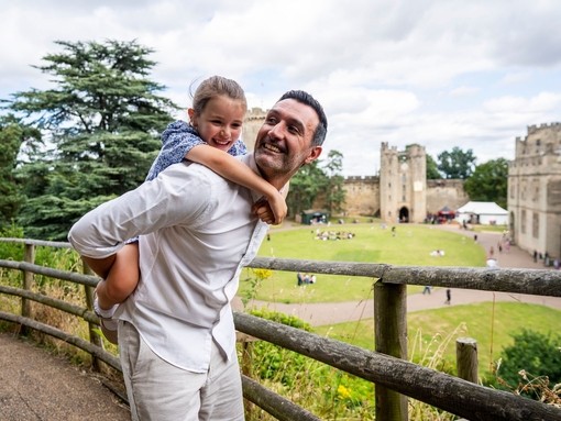 A man holds his daughter on his back in front of a heritage castle