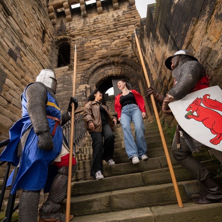 Two women explore a castle while two men stand in medieval costume