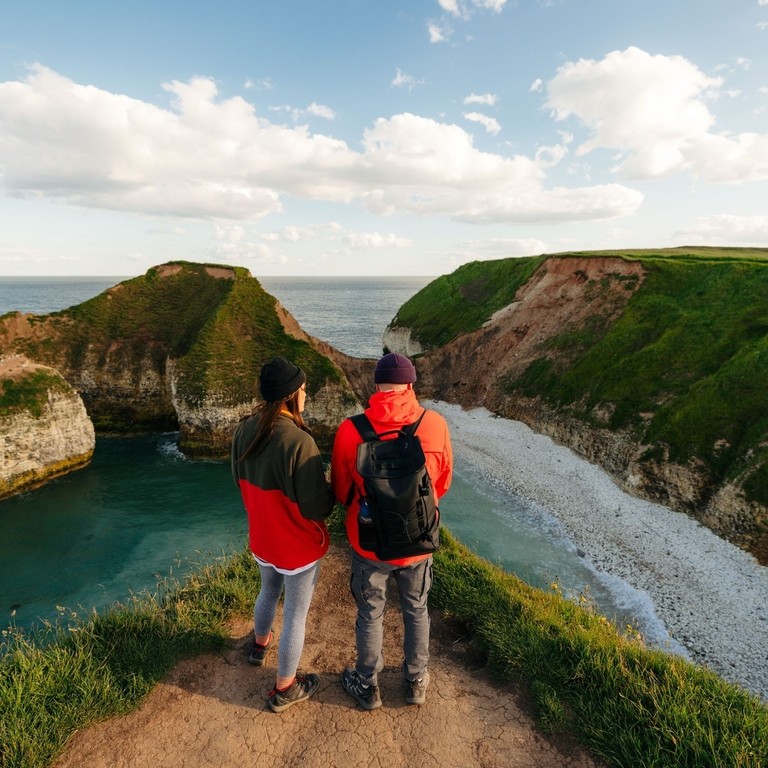 A man and woman stand on a cliff edge in front of a sea view